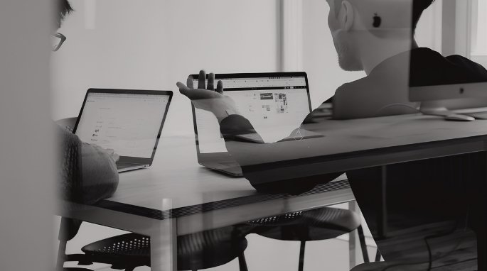 Dos profesionales con portátiles revisando contenido en pantalla durante una reunión de trabajo, en blanco y negro